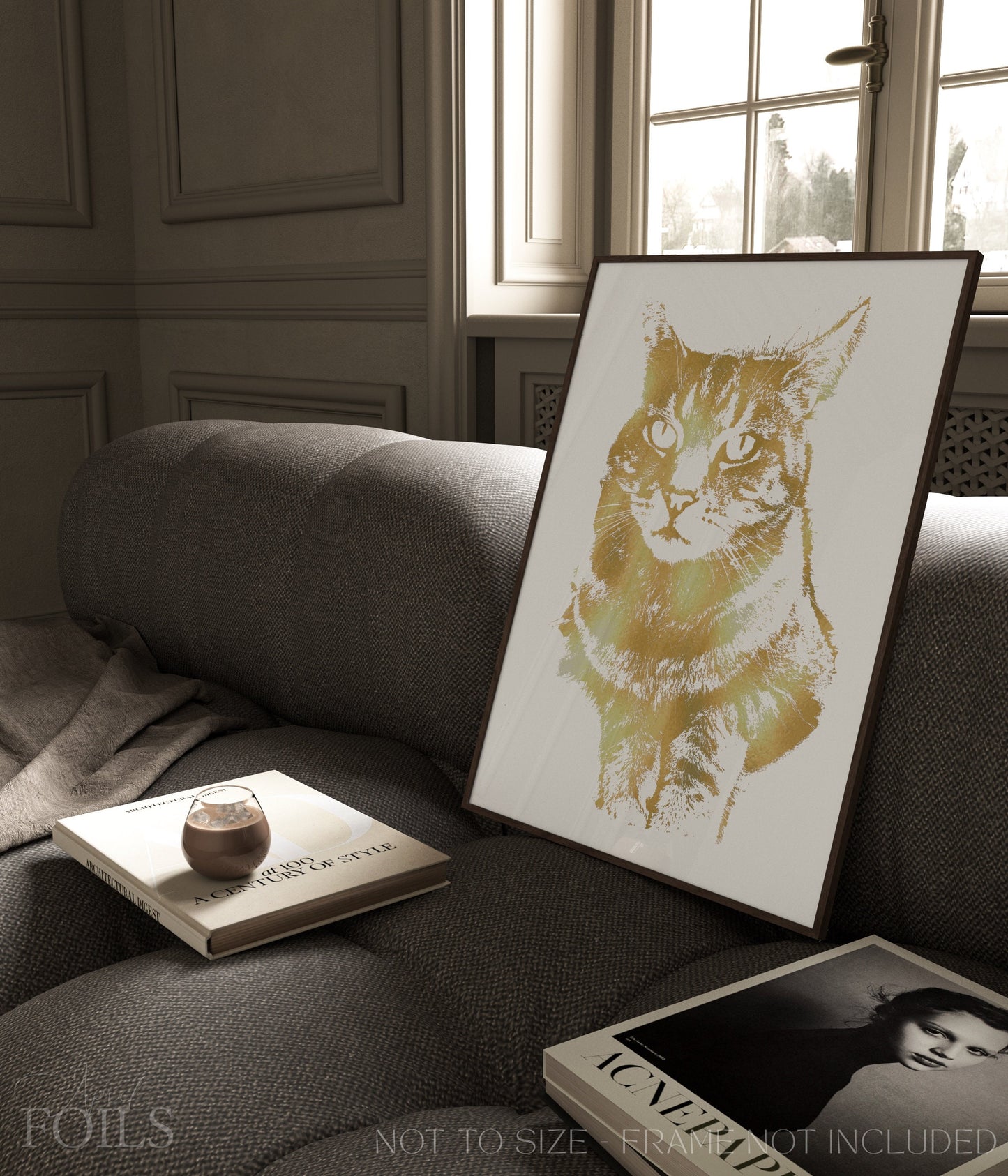 Framed foiled artwork of a pet cat on a sofa with a book and a small object.