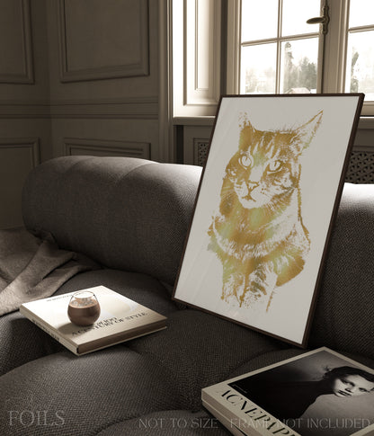 Framed foiled artwork of a pet cat on a sofa with a book and a small object.
